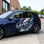 Side view of a dark blue car with a Layer Up Labs logo decal and geometric design on the door